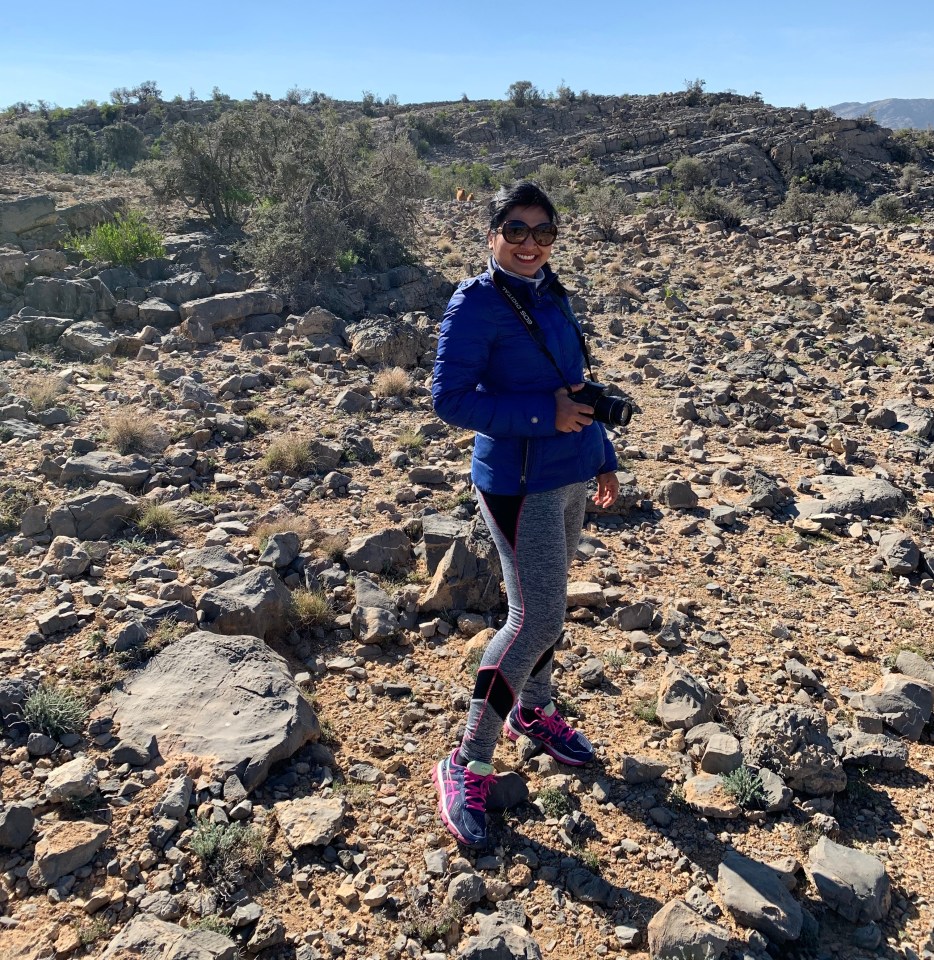 Woman hiking in rocky terrain, holding a camera.