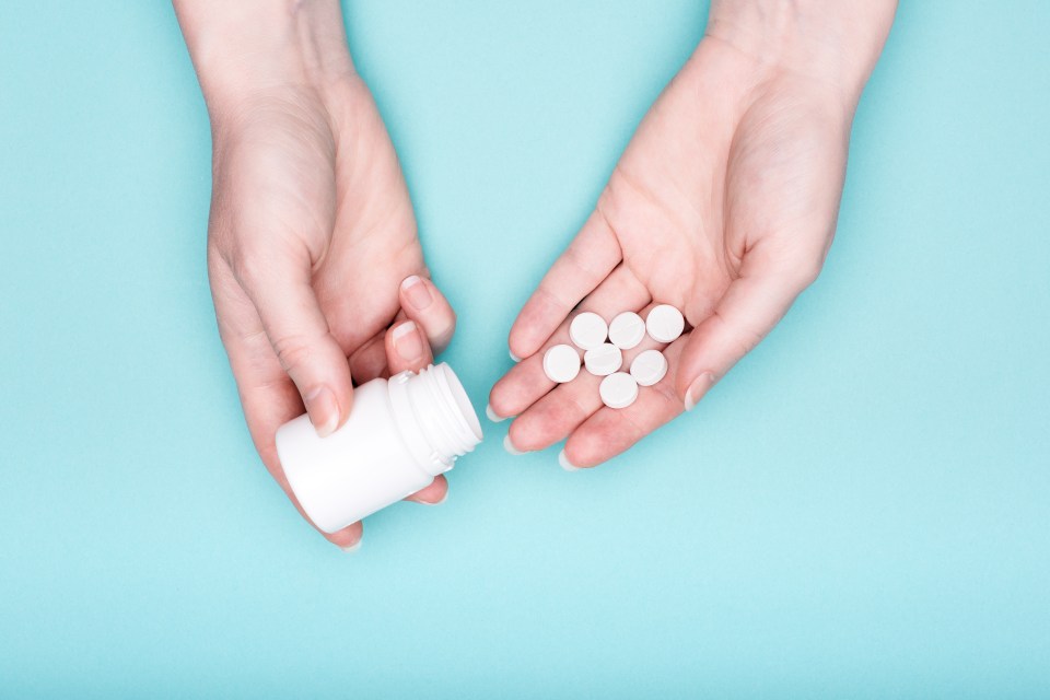 Woman's hands holding pills and a medicine bottle.