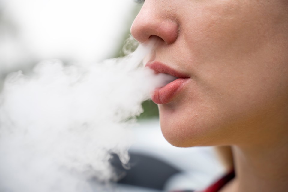 Close-up of a young woman exhaling vapor from an e-cigarette.