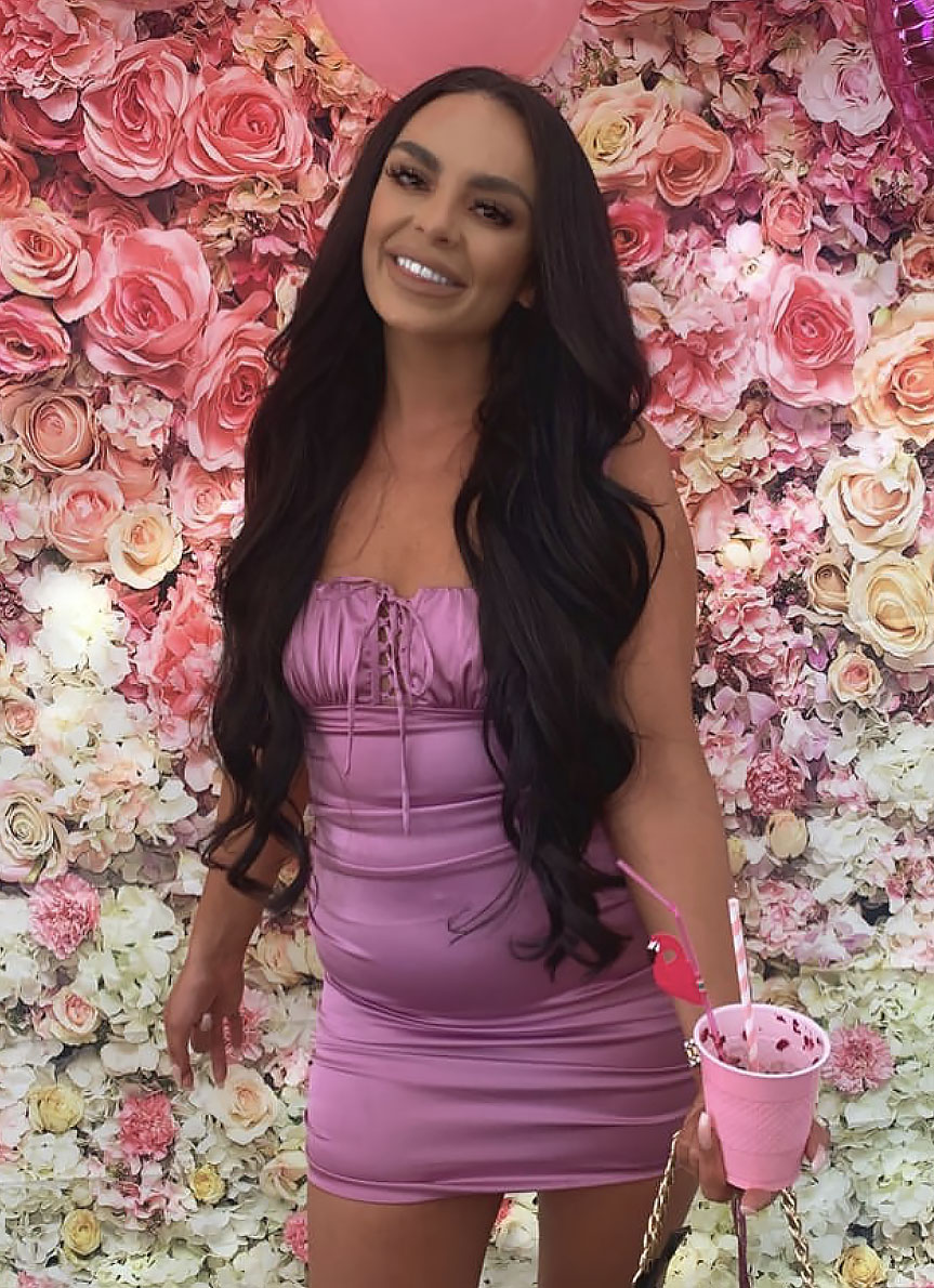 Woman in purple satin dress in front of flower wall.