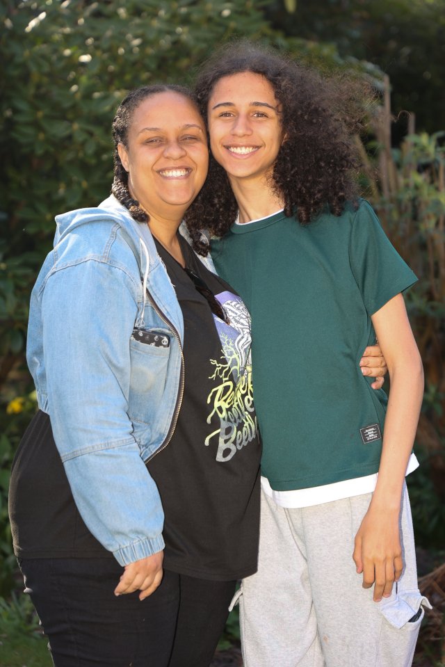 A mother and son stand close together, smiling.