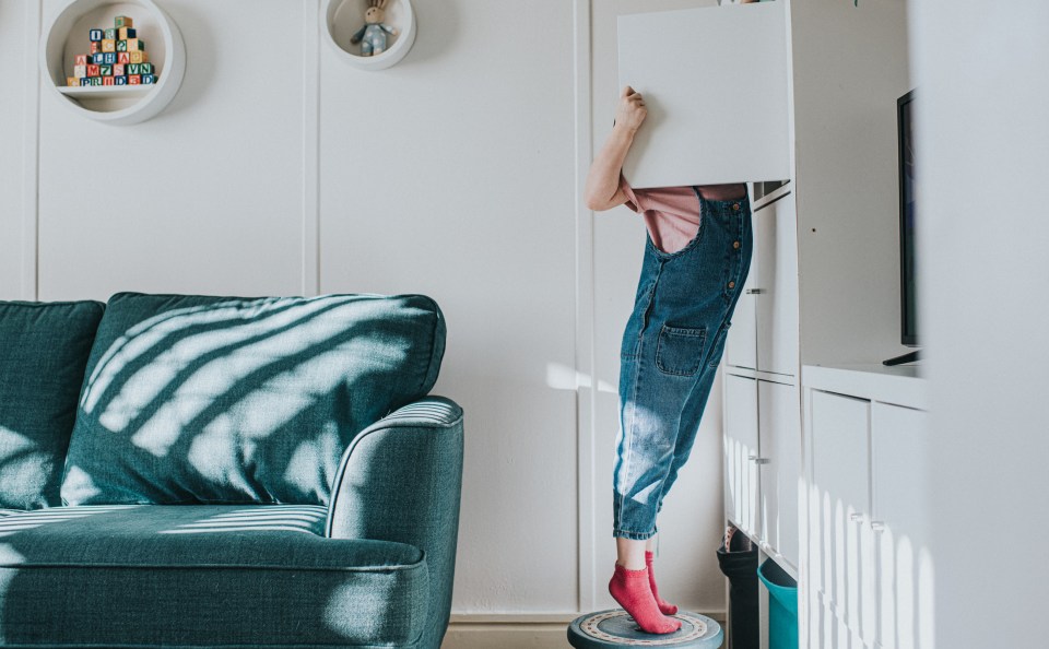 Girl standing on stool to reach high cupboard.