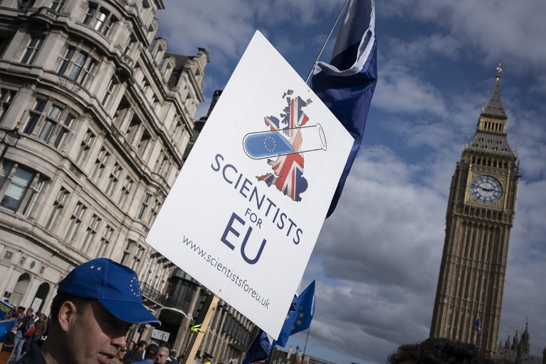 A man in a blue cap with the EU flag on it, holds a sign that reads "Scientists for EU"