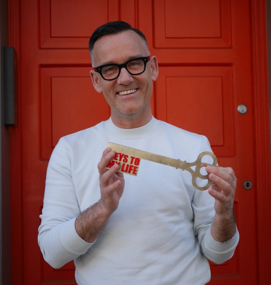 Brendan Courtney holding a large key with "Keys to My Life" written on it in front of a red door.