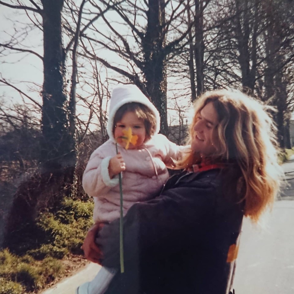 A father holding his young daughter who is holding a daffodil.