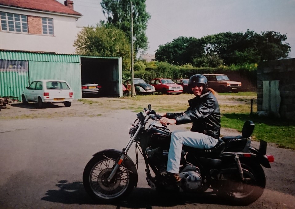 Man on motorcycle in front of garage and cars.