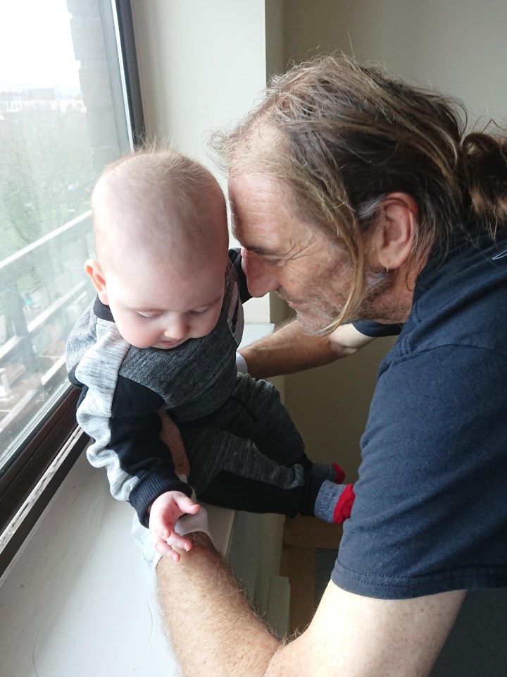 A man holding his baby by a window.