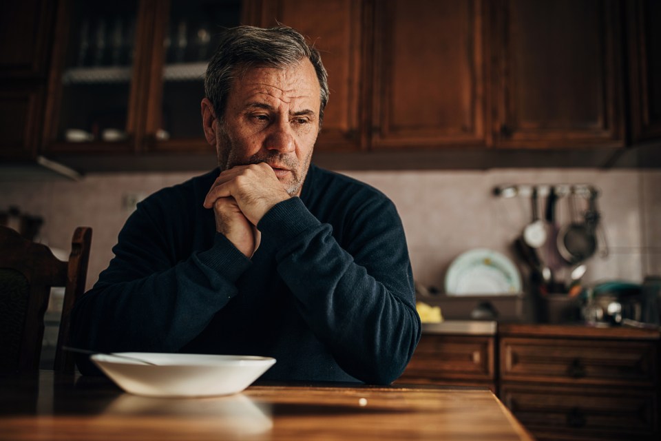 Depressed man sitting at a table with an untouched bowl of food.