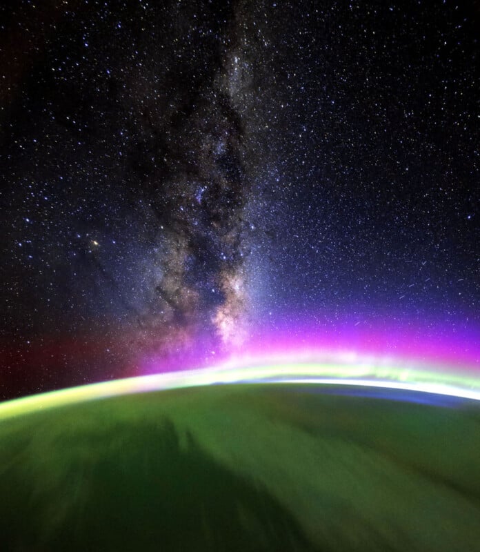 A view from space showing Earth’s curved horizon with green and purple auroras, and the Milky Way galaxy visible in the star-filled sky above.