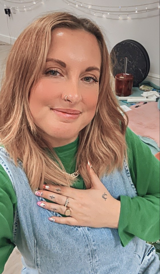 Woman with blonde hair and a green shirt holding her hand to her chest.