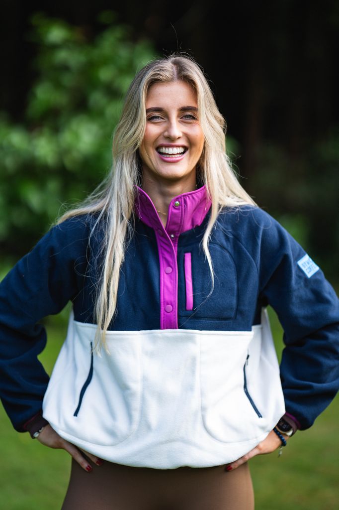 blonde woman in a navy and white jumper with her hands on her hips smiling 