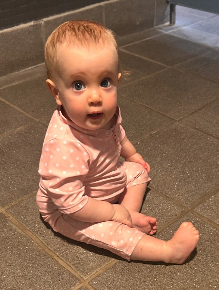 Baby girl sitting on the floor wearing a pink polka dot swimsuit.