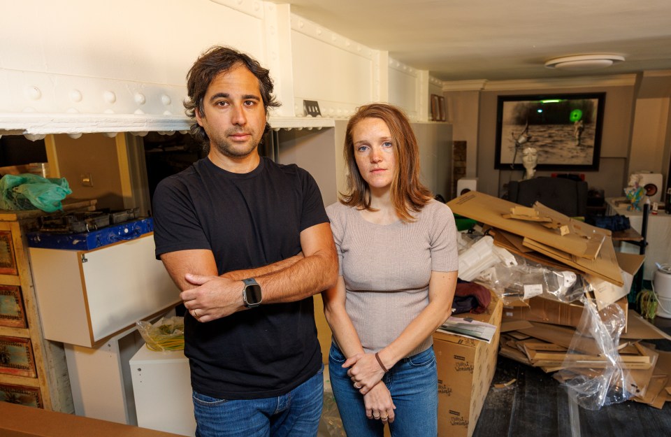 A couple stands in their messy, unfinished apartment.