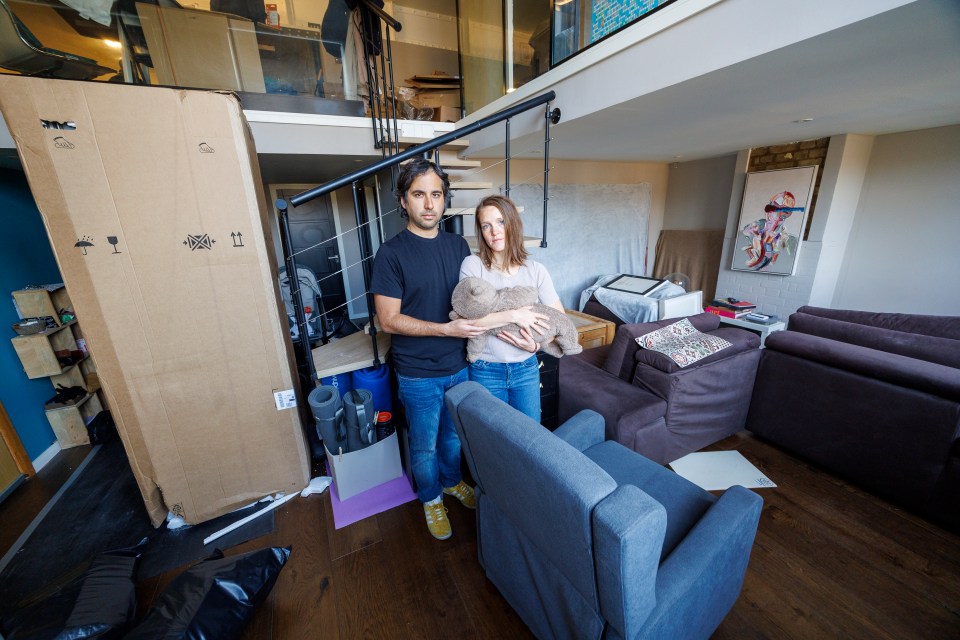 Parents holding baby in messy apartment.
