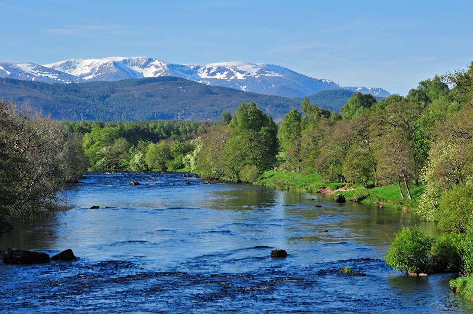 River Spey flowing through a lush green valley with snow-capped mountains in the background.