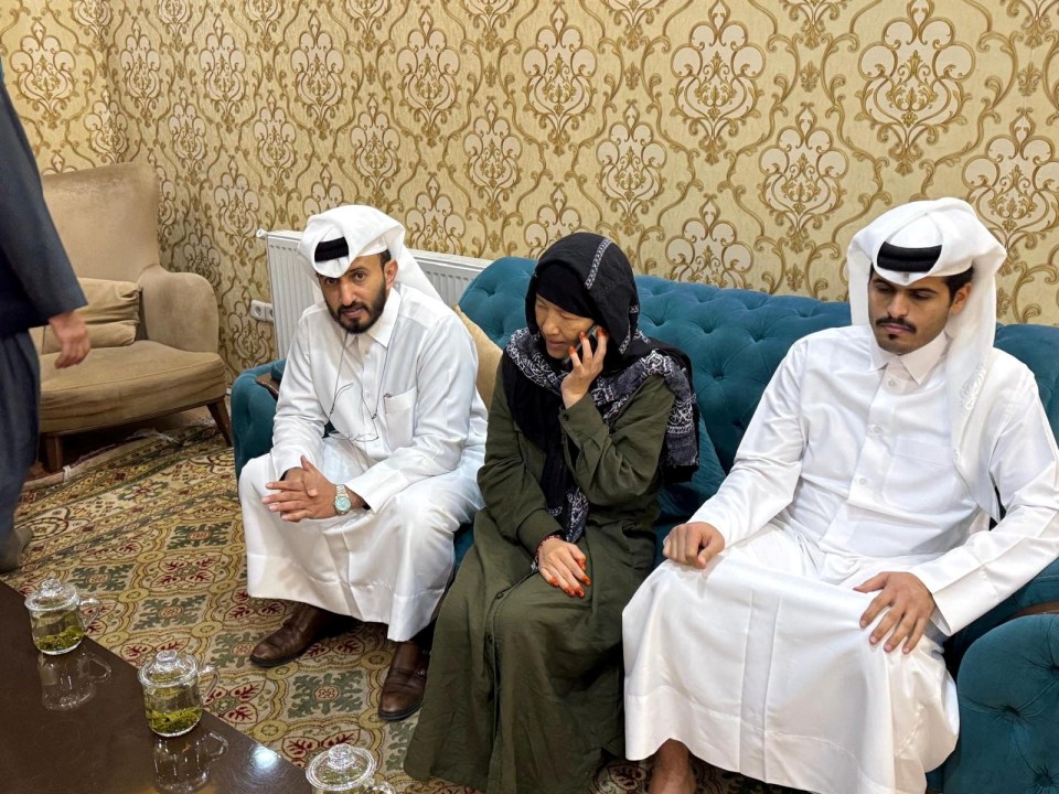 A woman on a phone call sits between two men in traditional Qatari clothing.