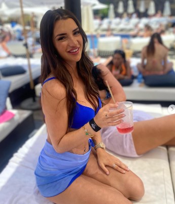 Woman in blue bikini and sarong holding a drink.