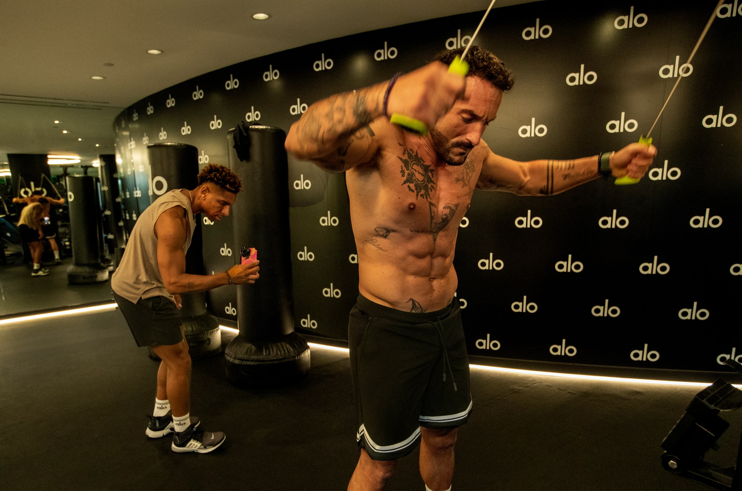One muscled man exercising while another records him.