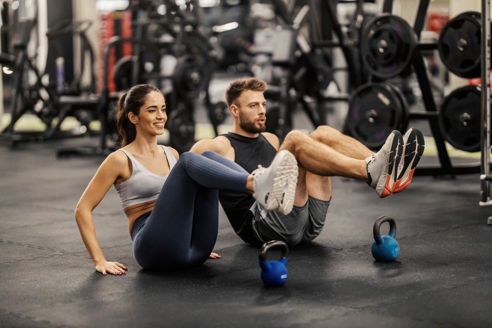fit sporty couple is doing exercises for abs while sitting on a gym floor.