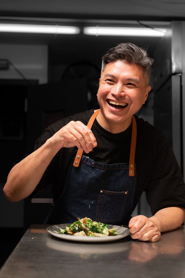Smiling chef seasoning a plate of food.