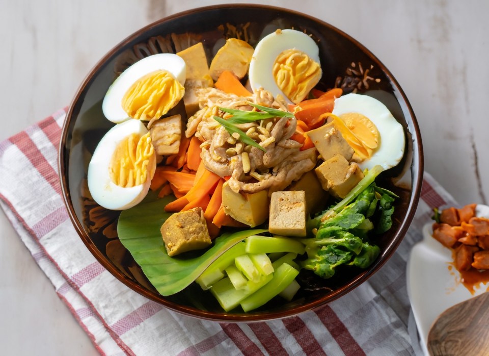 Bowl of food with eggs, tofu, carrots, and greens.