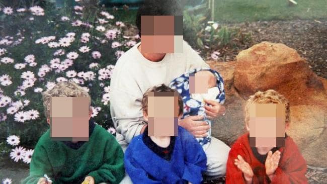 Photo of a woman and four children with their faces blurred, in front of a flowerbed.