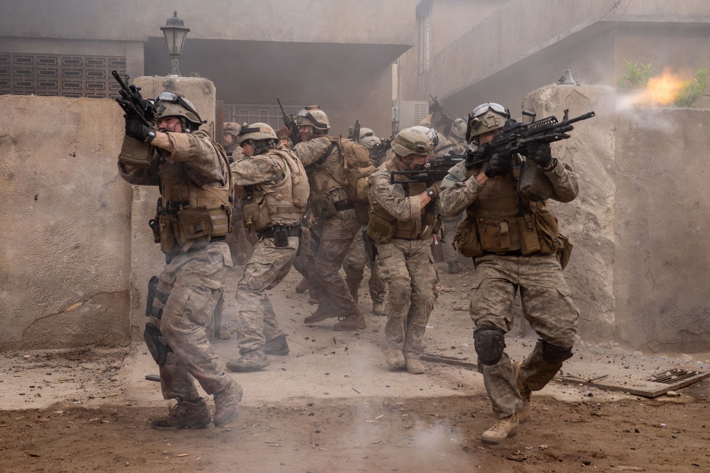 Several Navy SEALs walk out of a gate firing assault rifles in the movie Warfare