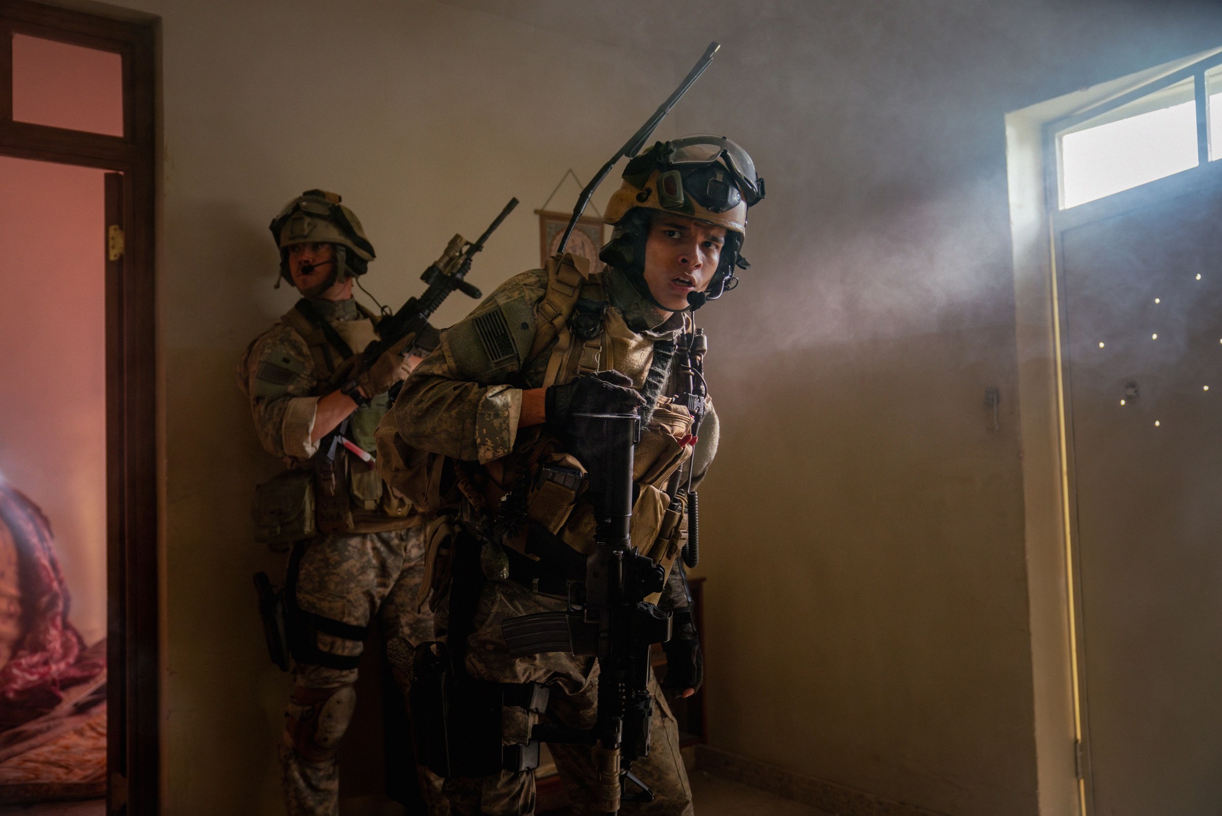 Two soldiers in the movie Warfare hold weapons while standing near a door with bullet holes in it