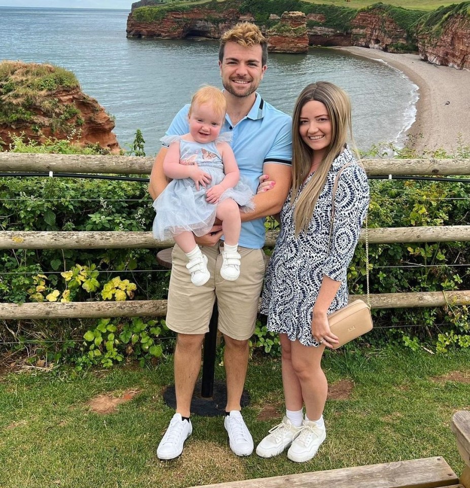 Family photo of a mother, father, and baby girl near the ocean.