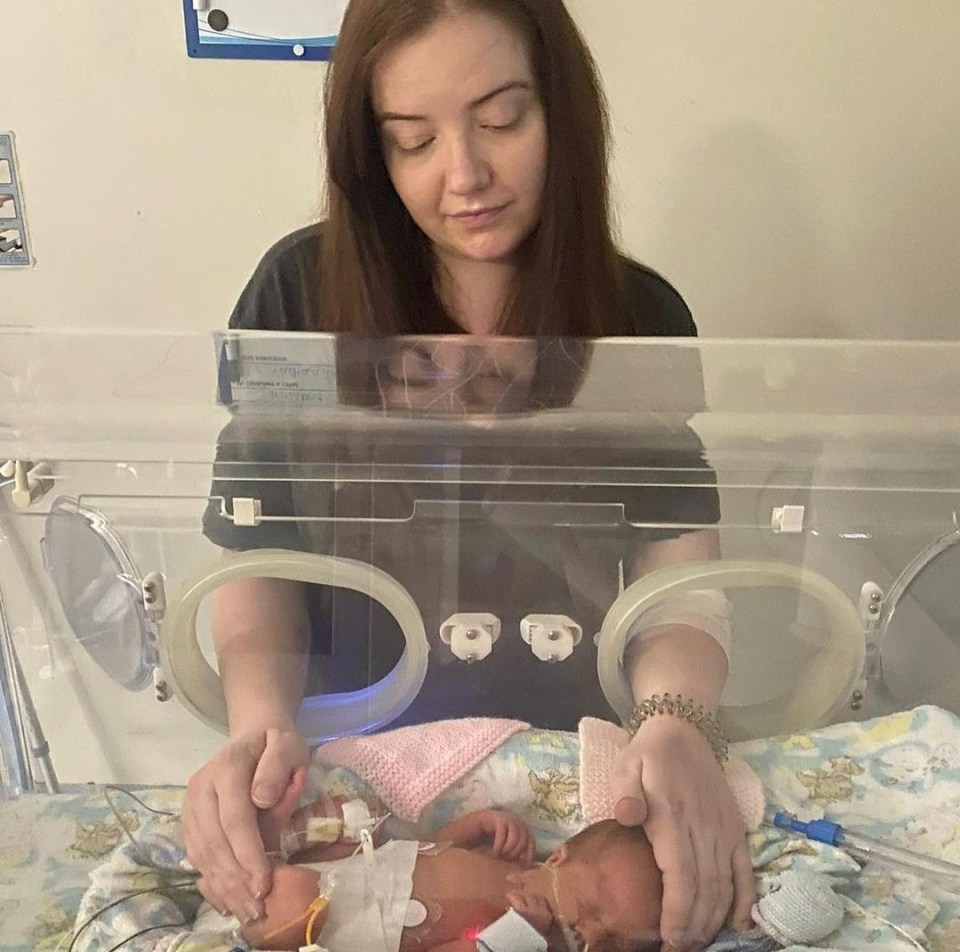A mother gently touches her premature baby in an incubator.