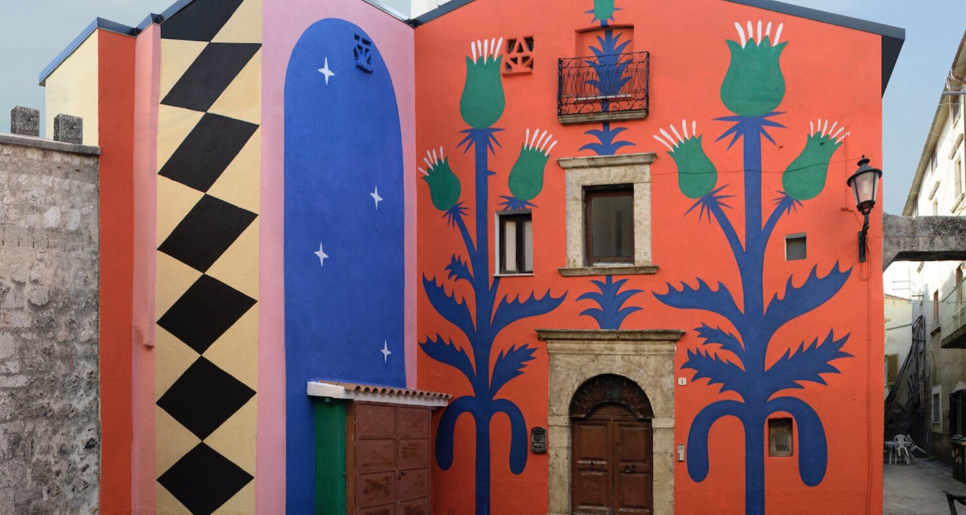 part of a mural on a two-story building in Italy, with a red background and geometric patterns and thistle designs