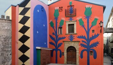 part of a mural on a two-story building in Italy, with a red background and geometric patterns and thistle designs