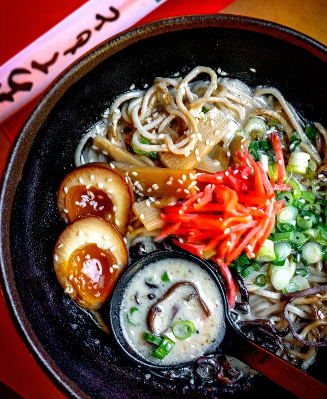 Bowl of ramen with soft boiled eggs, pickled ginger, and sesame seeds.
