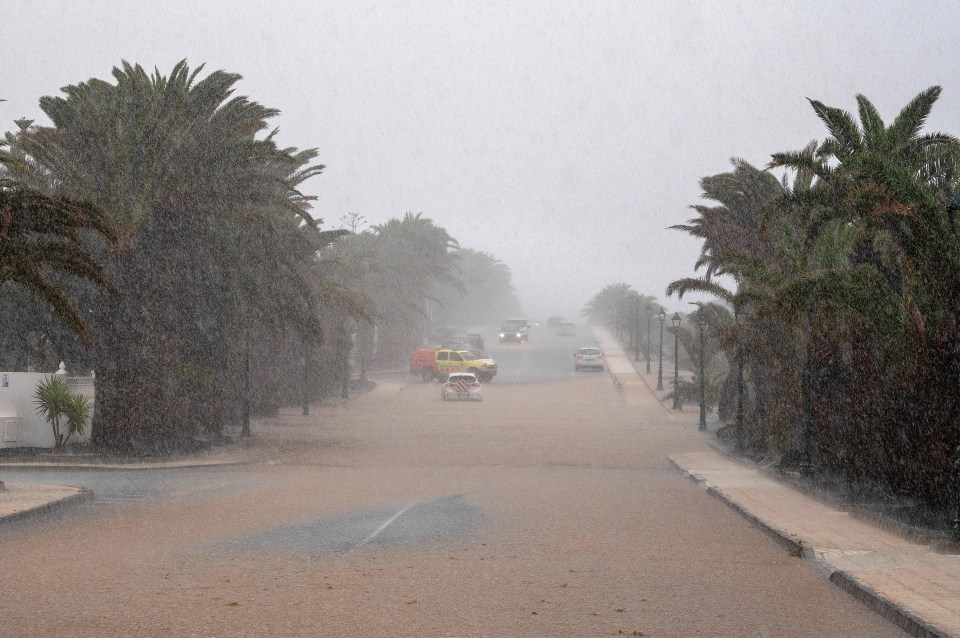 Flooded street with cars driving through heavy rain.