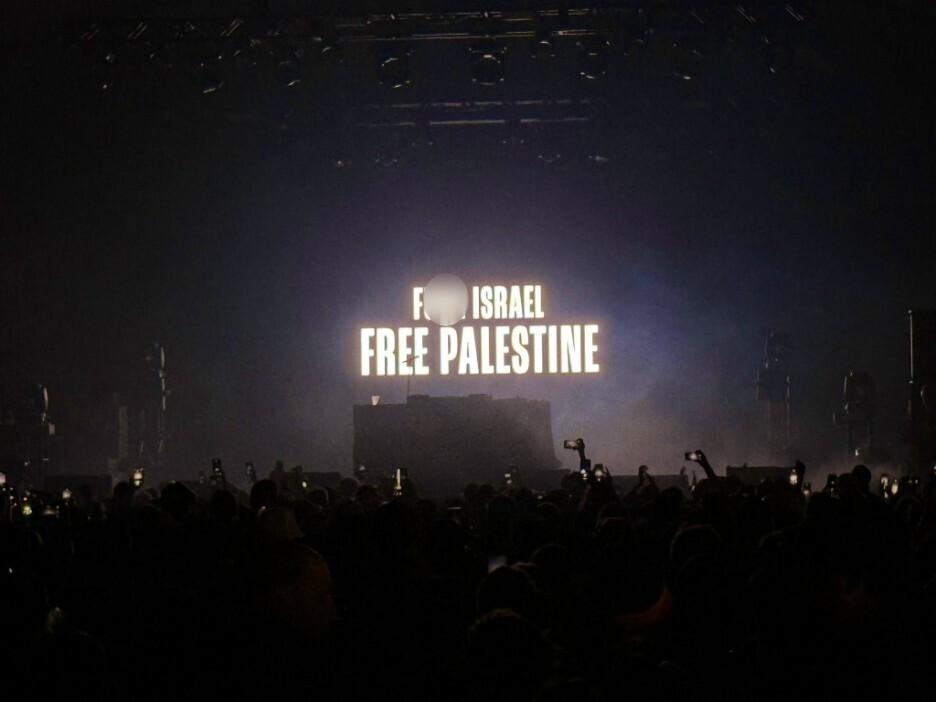 Crowd at concert with "Free Palestine" sign on stage.