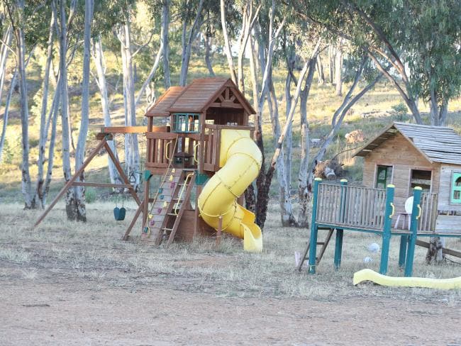 Wooden playground set with yellow slide in a wooded area.