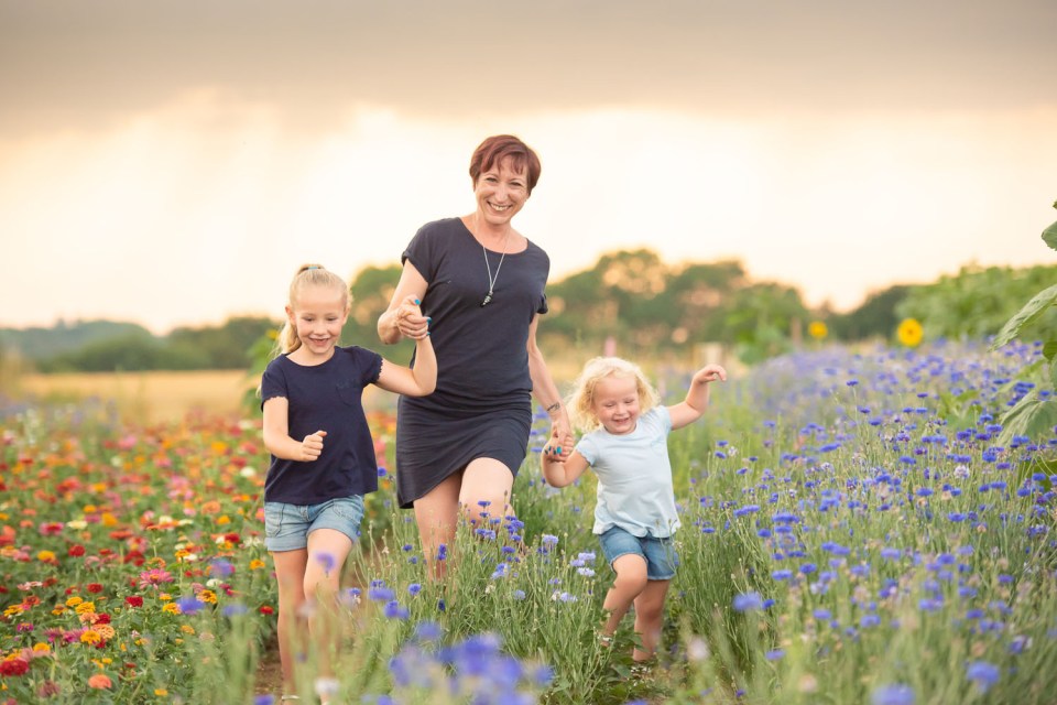Woman walking through a flower field holding hands with two young girls.