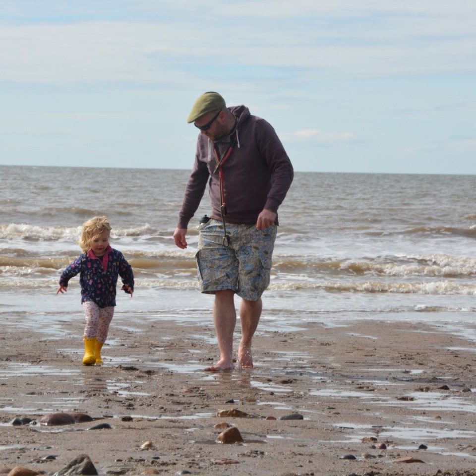 A man and toddler walk on a beach.