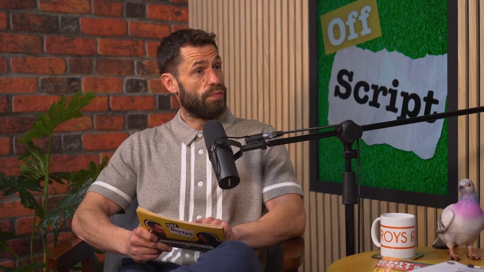 kelvin fletcher on off script video podcast, wearing a grey t shirt and sitting in a chair with a microphone in front of him