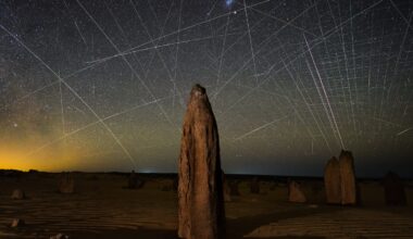 light streaks in the night sky above an arid landscape with rocky forms