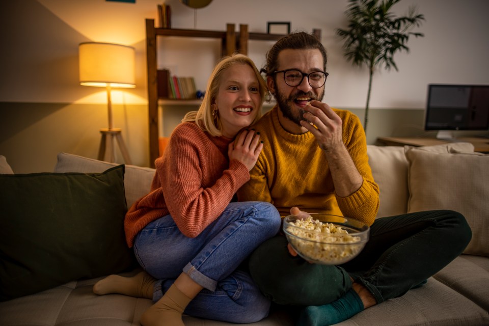 Couple cuddling on couch, eating popcorn and watching TV.