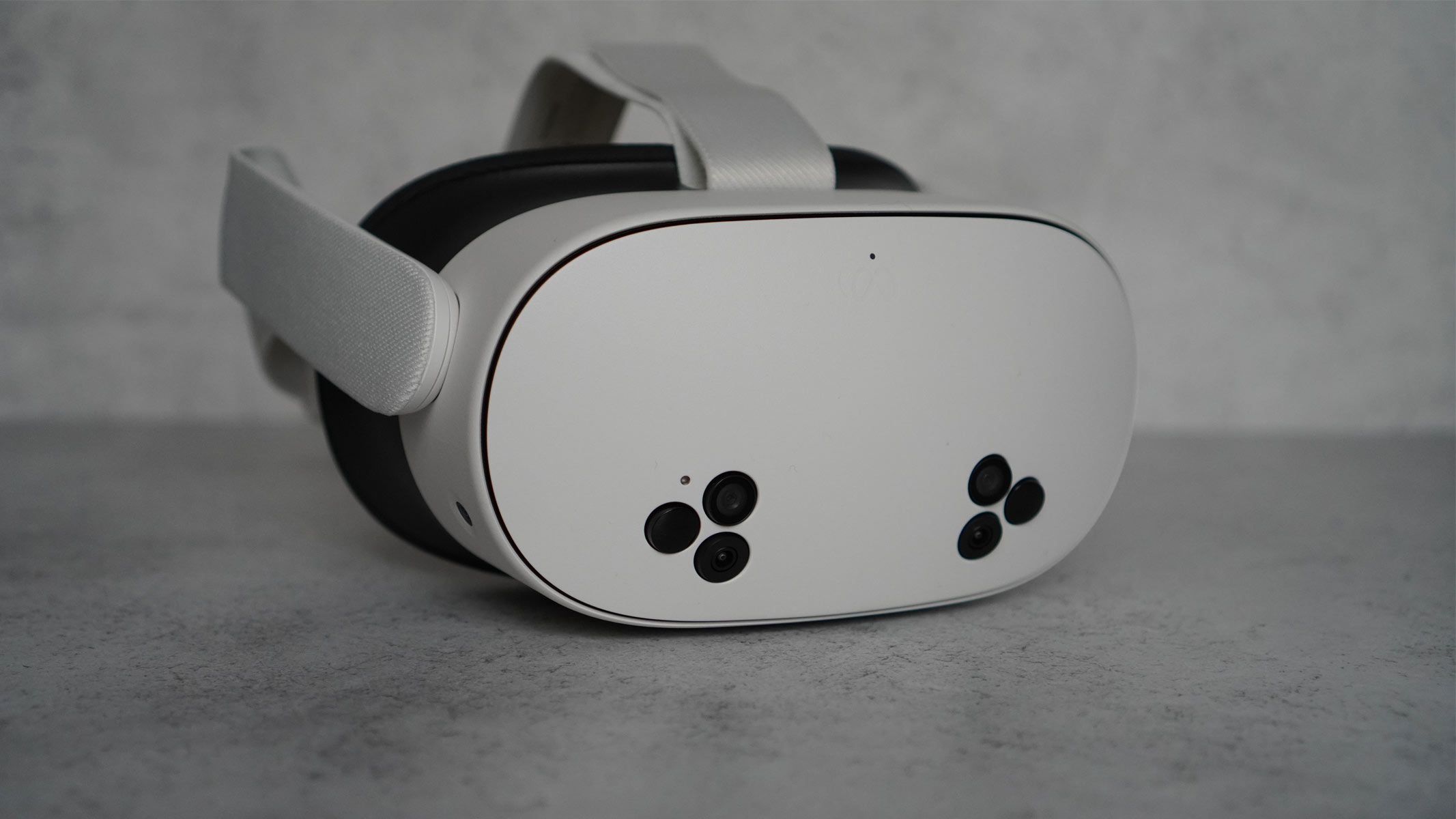 The Meta Quest 3S is a white headset with black cameras on the front and white controllers on a gray background