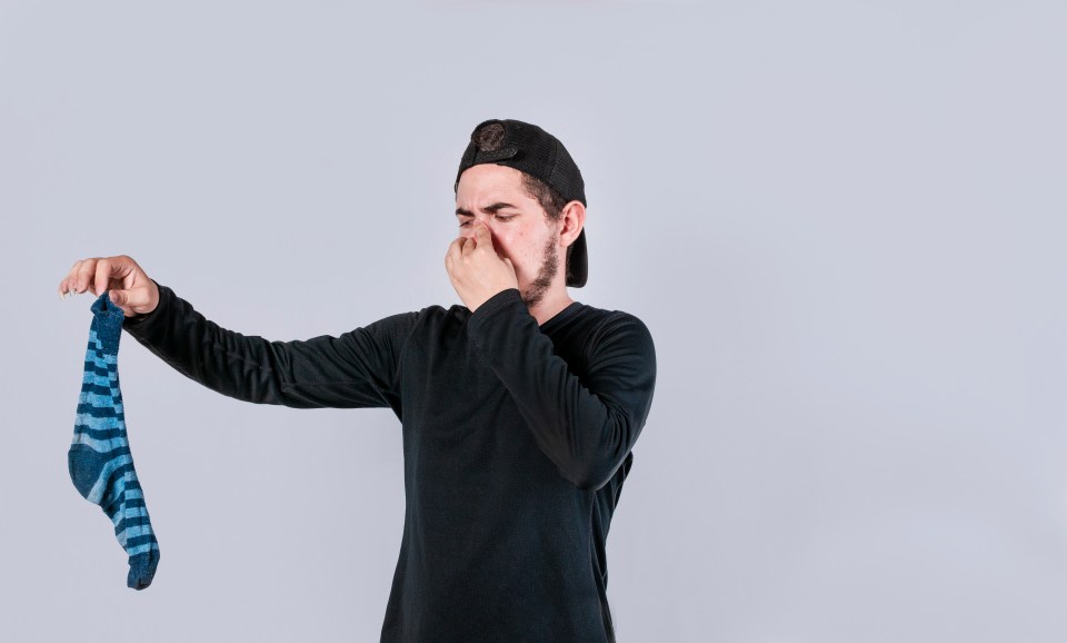 Man holding a smelly sock and pinching his nose.