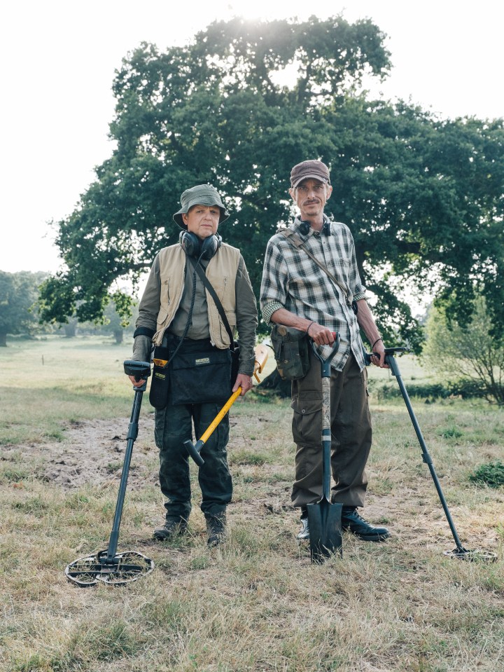 Two men metal detecting in a field.