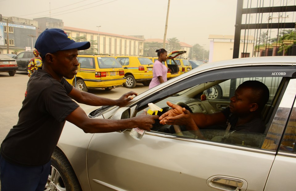 A Nigerian Civil Defence Corps official sanitizing a man's hands in Lagos.