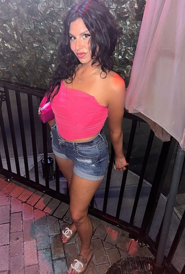 Woman in pink top and denim shorts.