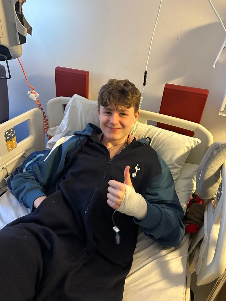 Teenage boy in hospital bed giving thumbs up, wearing a bandage.