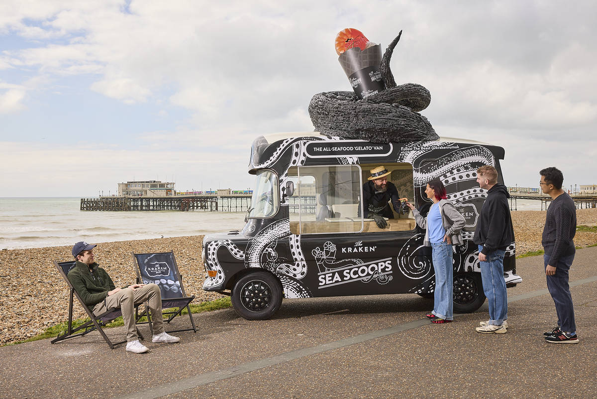 people queuing at fishy ice cream-style van at beach with one person sat on deckchair