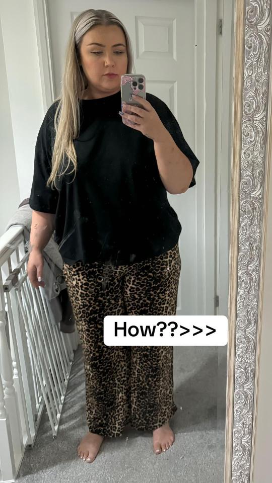 Woman in black top and leopard print pants taking a selfie in a mirror.