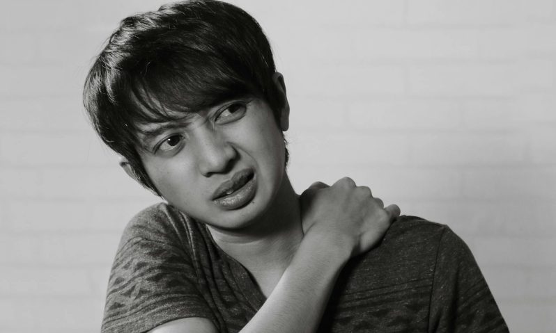 Man wearing a T-shirt holding his shoulder in pain from an injury